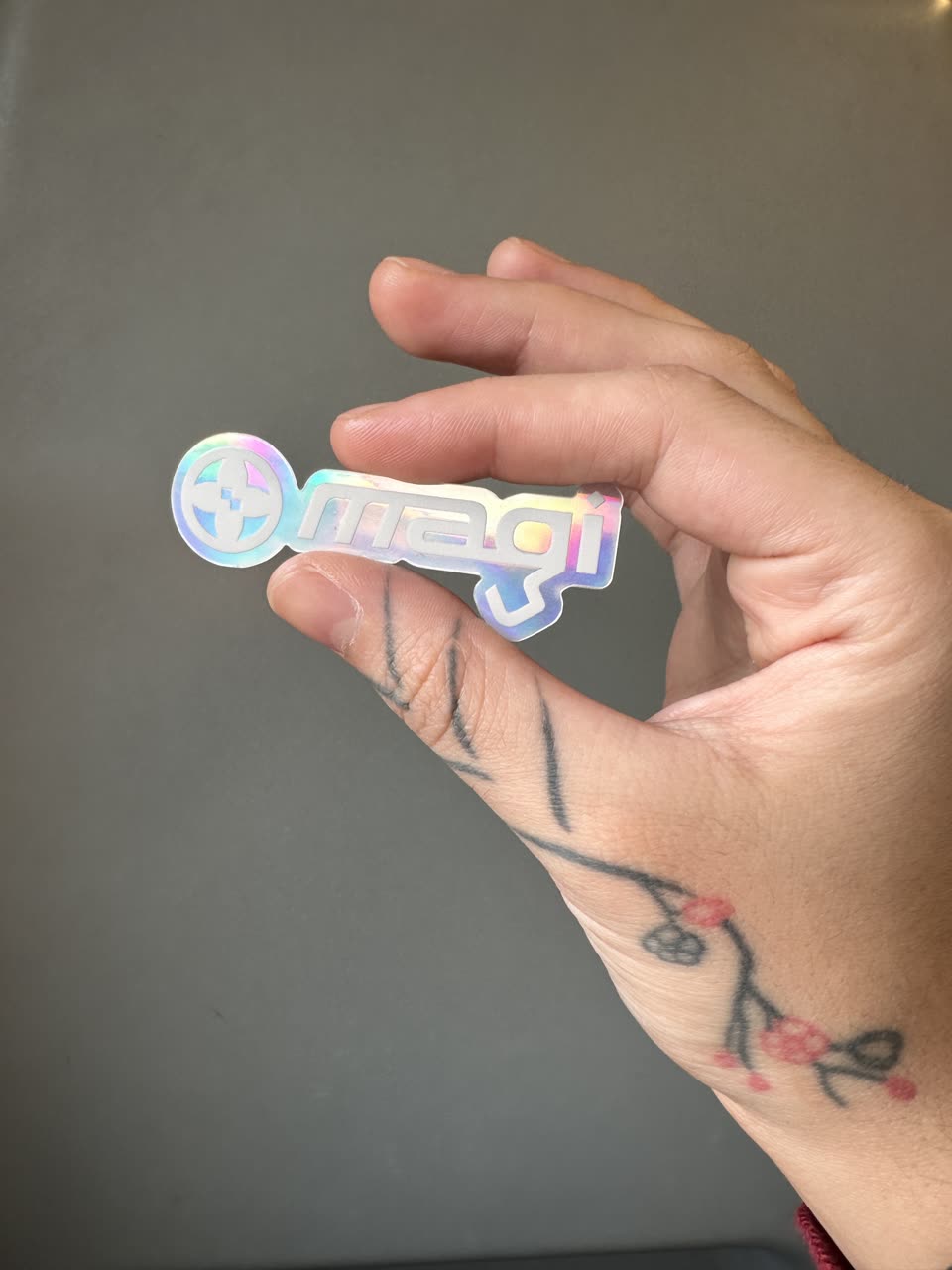 A hand holding the magi holographic sticker